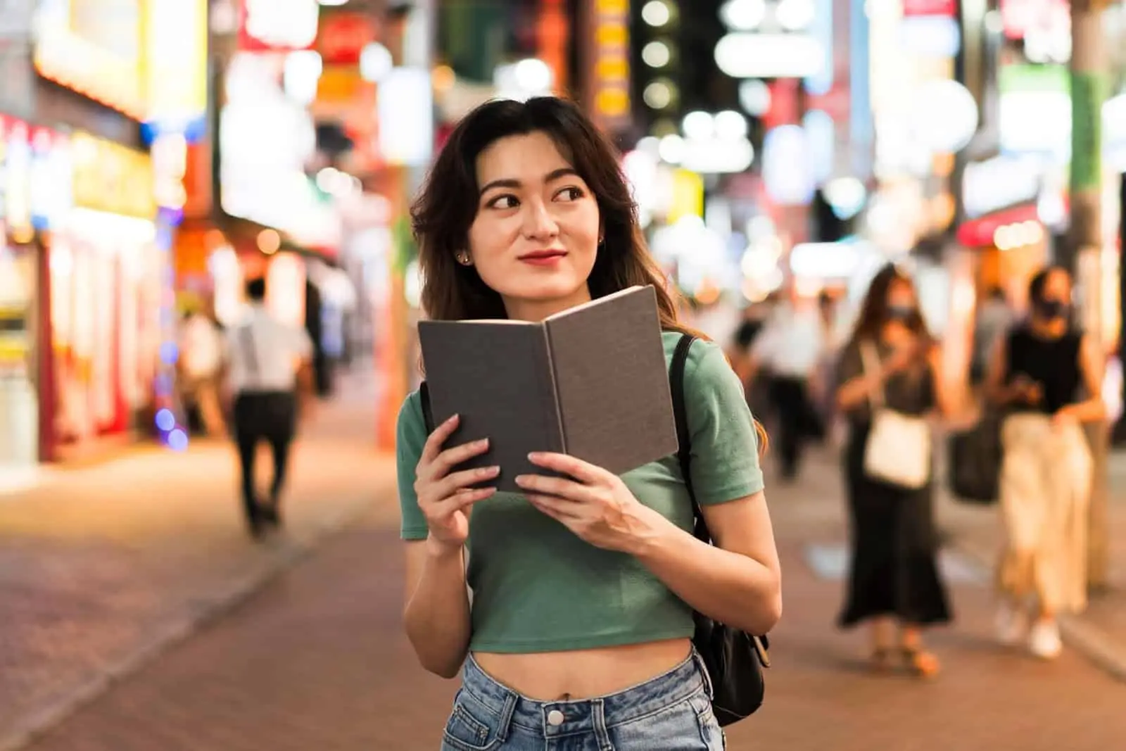 Charming woman exploring vibrant city streets in China, holding a guidebook; bustling nightlife scene ideal for travel and cultural discovery.