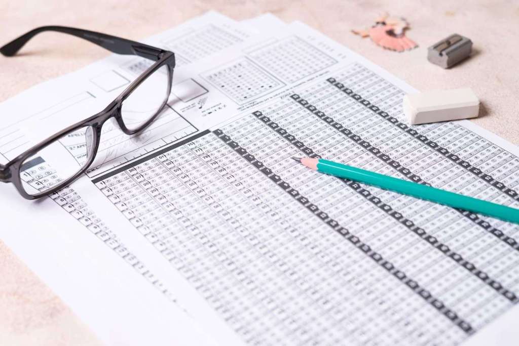 Eyeglasses resting on a completed bubble sheet for a standardized test or exam, with a green pencil, erasers, and test-taking accessories nearby. Focus on exam preparation and application processes for studying in China.