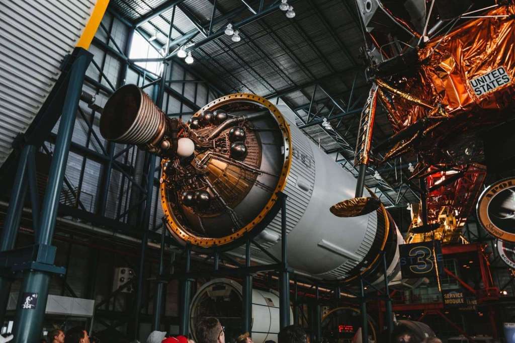 Detailed view of a commercial space rocket module inside a large, high-ceilinged hangar with visitors observing, highlighting space exploration technology and US space programs.