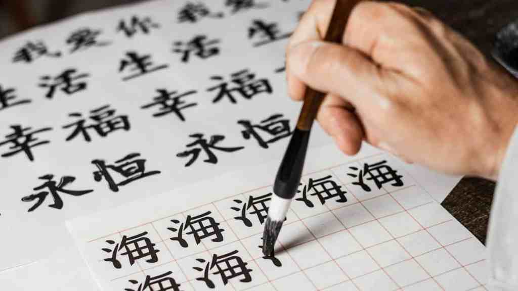 Hand practicing Chinese calligraphy with black ink characters on paper, focusing on the word 'Hǎi' (sea) in traditional brush writing, ideal for students and learners applying for China programs.