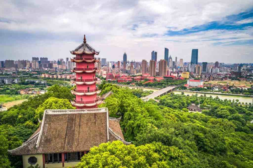 Beautiful traditional pagoda surrounded by lush green trees with modern Shanghai skyscrapers in the distance, illustrating China’s blend of ancient culture and modern development.