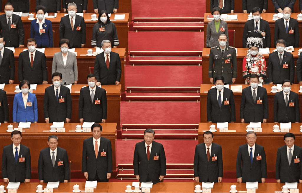 A formal gathering of officials seated in rows, wearing masks, with a focus on a podium in the foreground, showcasing a significant political event.