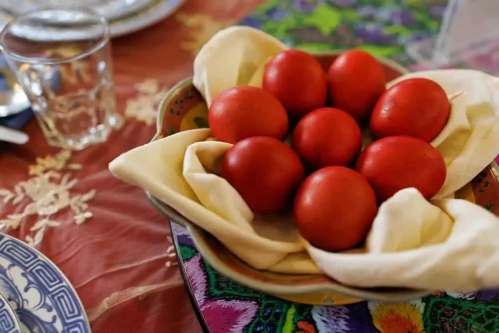 A bowl with eight red eggs arranged in a decorative cloth on a colorful table setting.