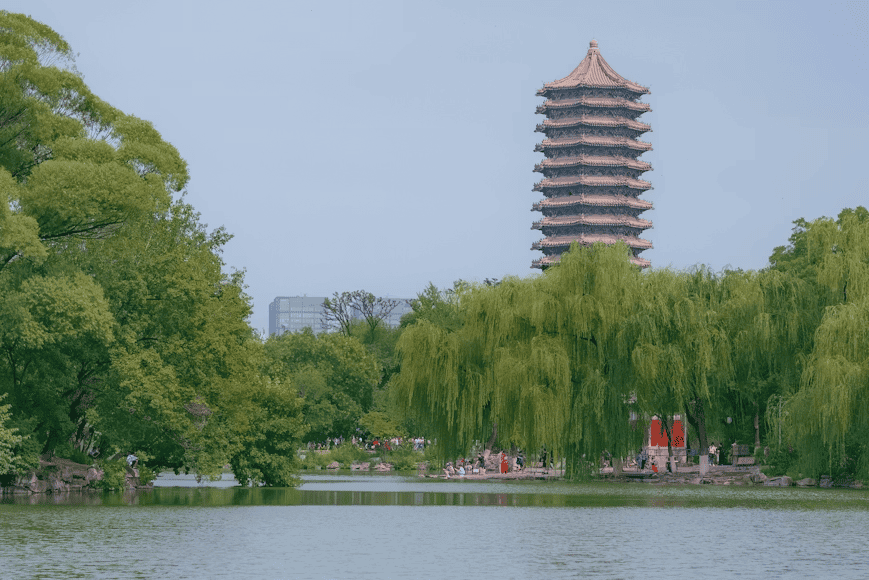 a tall tower towering over a lake surrounded by trees in Peking University, Beijing, China