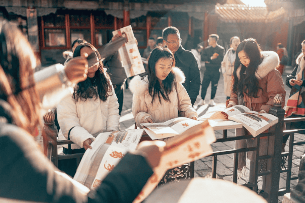 A group of people outdoors, looking at brochures and navigating an area with historical significance, dressed in winter coats, with one person holding a pamphlet towards the camera. 
