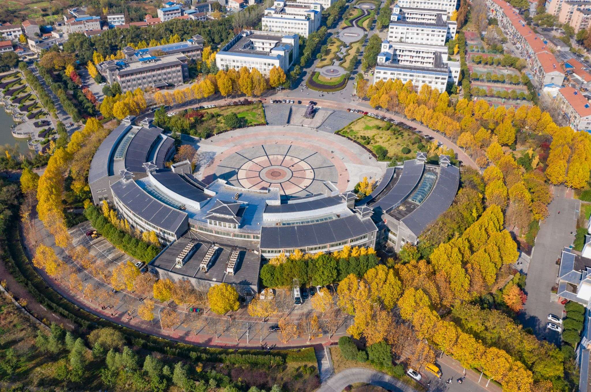 Aerial view of a modern building surrounded by landscaped gardens and autumn-colored trees, featuring a circular central plaza.
