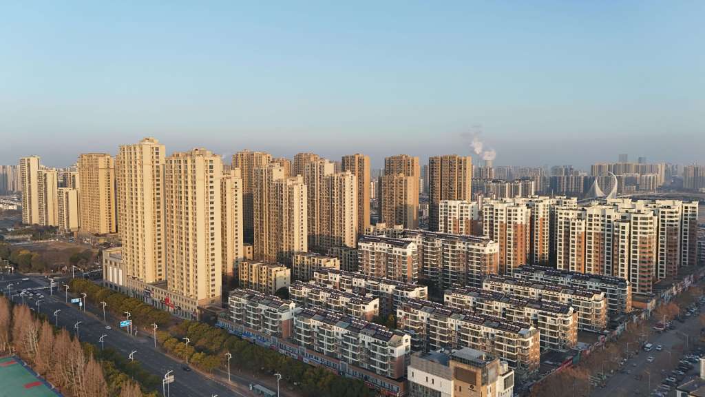 Aerial view of a modern urban landscape featuring tall residential buildings and a busy street lined with trees.