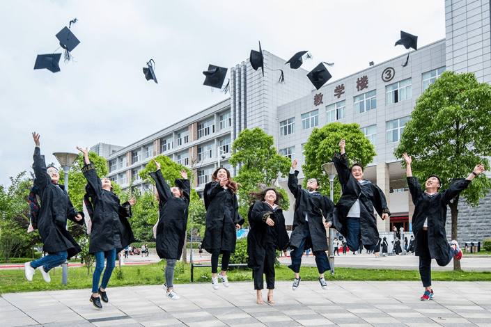 University graduates in black gowns jumping and tossing their caps in the air in front of a Chinese university building