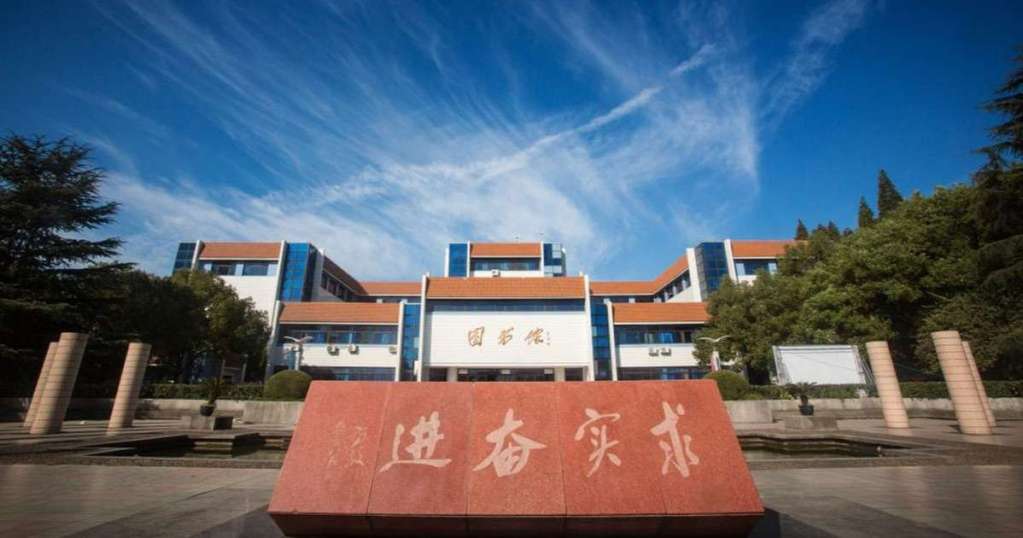 Jiaxing University campus in Jiaxing Zhejiang China building with blue glass and red-tiled roofs, featuring a stone monument in the foreground with Chinese characters, under a clear blue sky. 